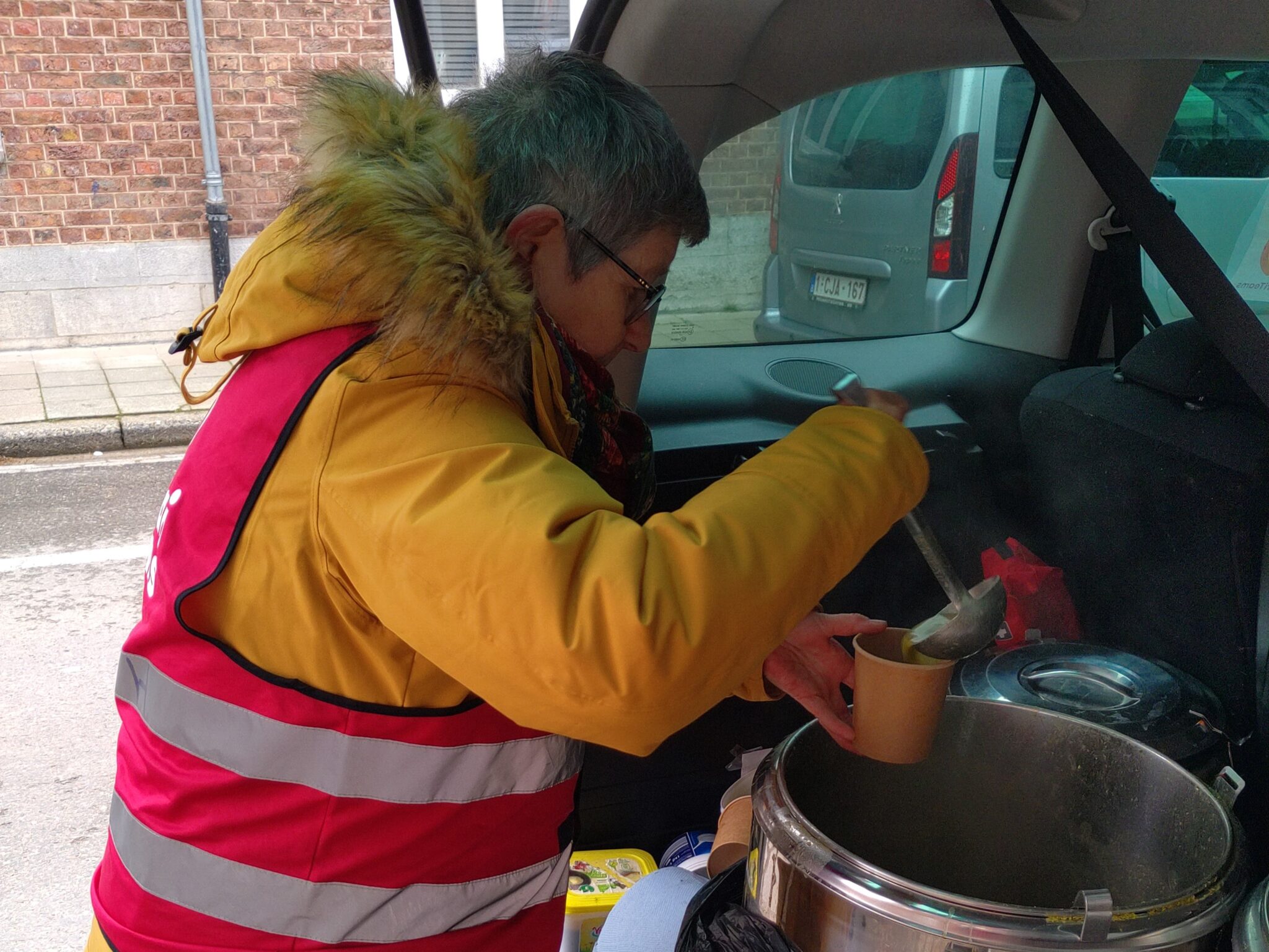 vrijwilliger met fluovestje aan schept soep uit in kofferbak van auto